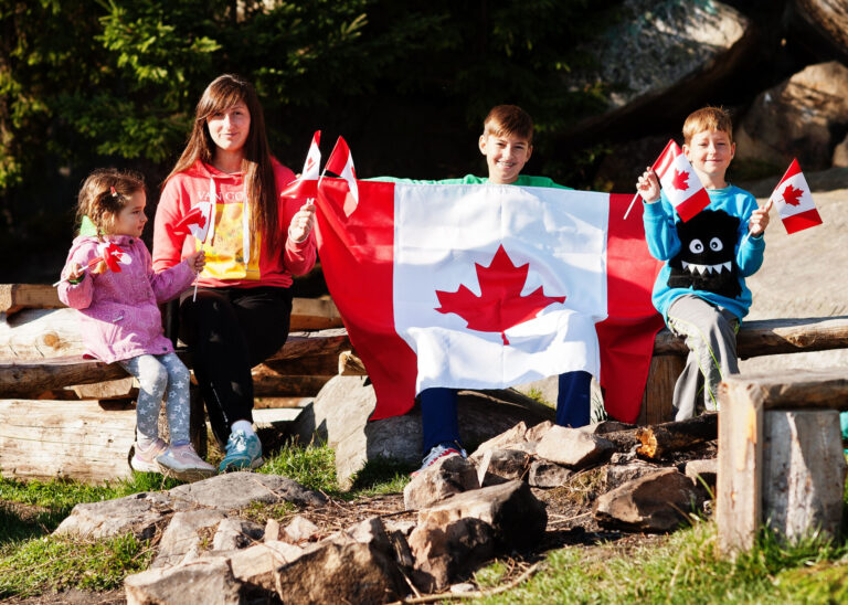 Happy Canada Day. Family of mother with three kids hold large Canadian flag